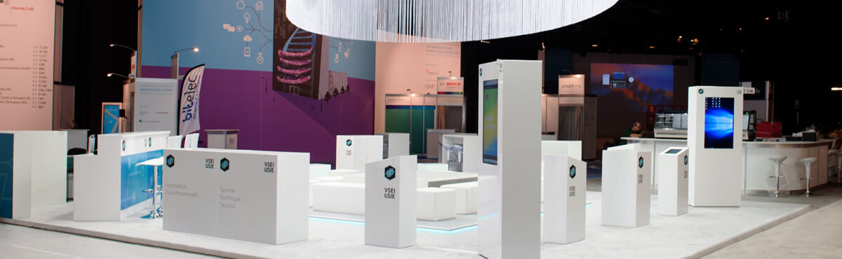 grosser messestand mit weissen mietmoebel wie theken mit logo branding und interaktiver tv station