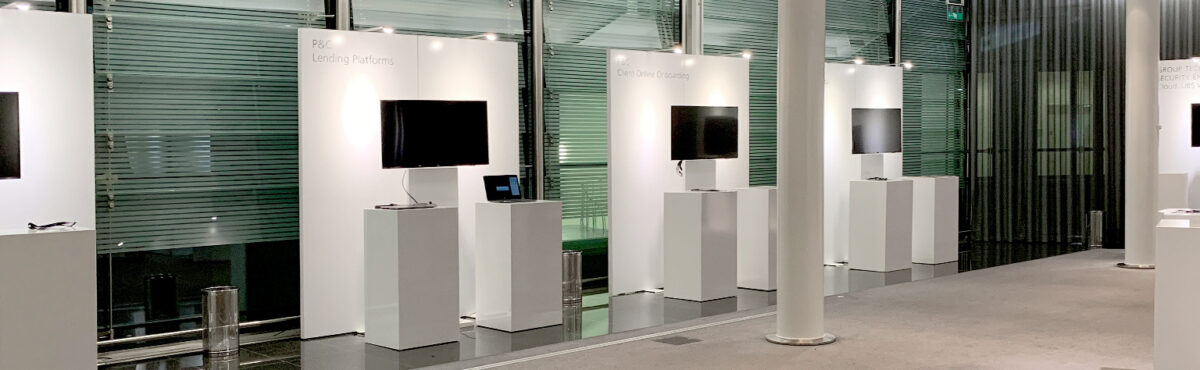 tv screens an einer messe mit beleuchteten rueckwaender und stehtischen in weiss